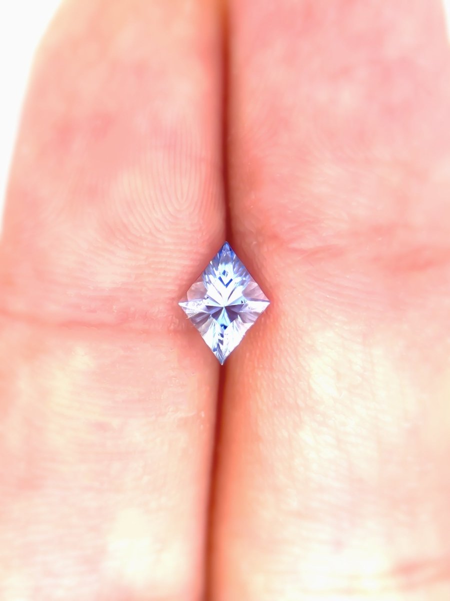 blue kite sapphire held between two fingers against two fingers for scale