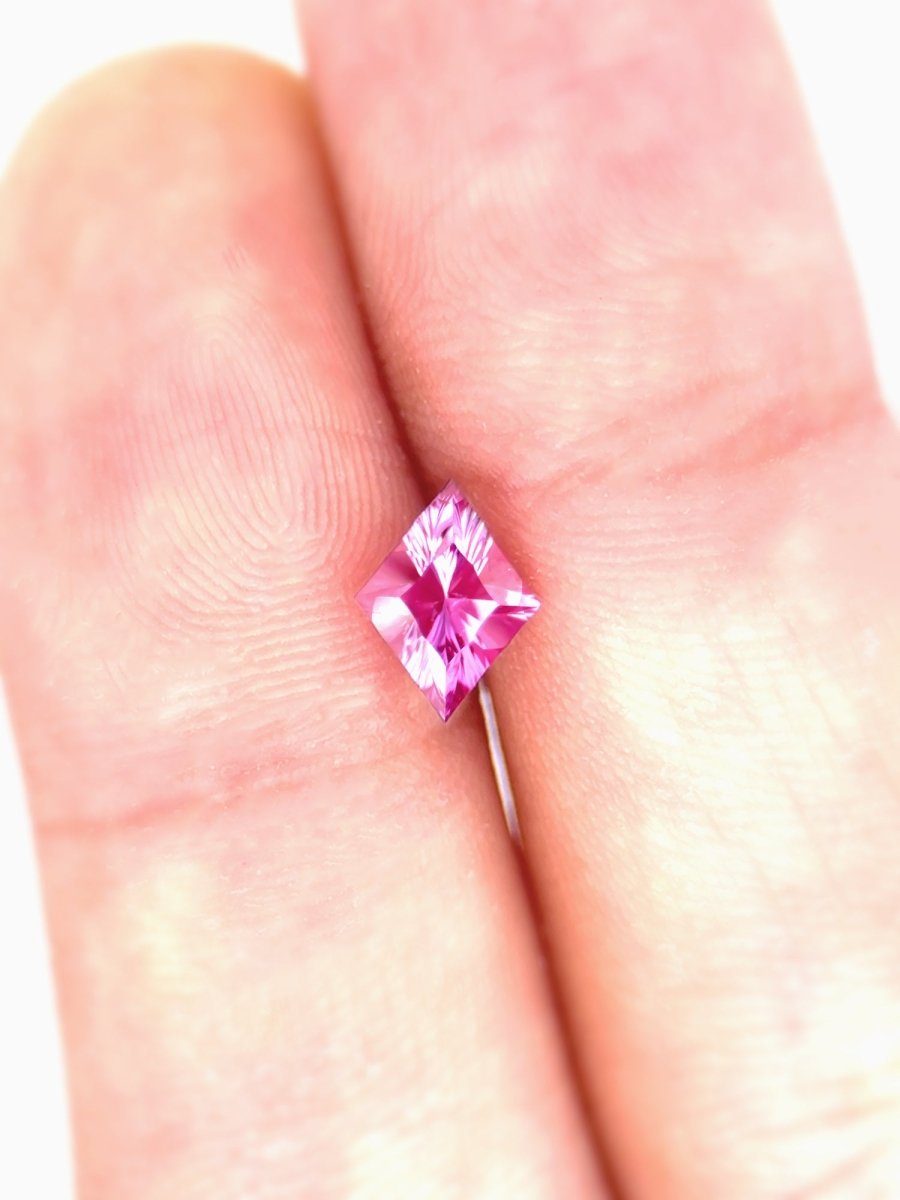 Pink sapphire held between two fingers against a white background for scale
