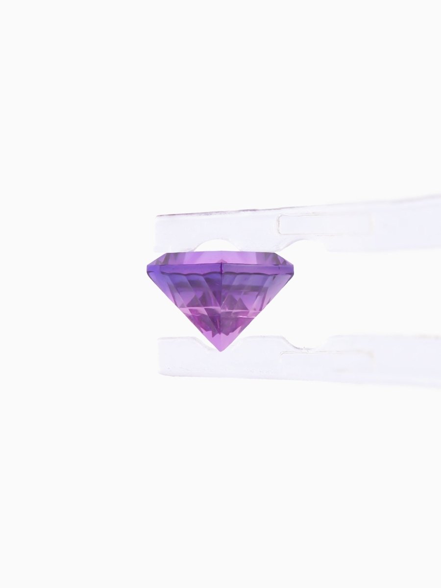 profile of purple sapphire held by tweezers on white background