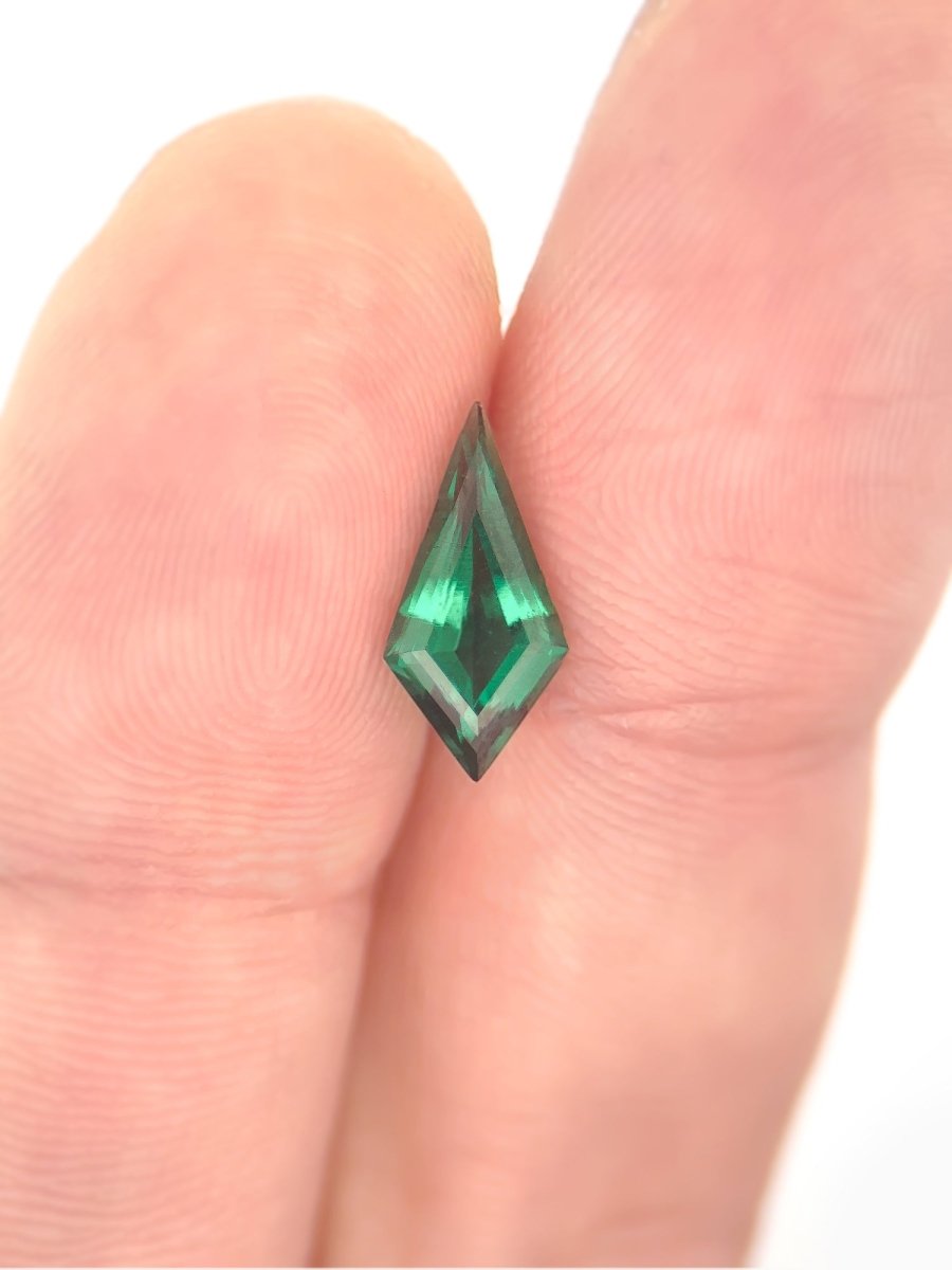 Green gemstone held between two fingers on a white background