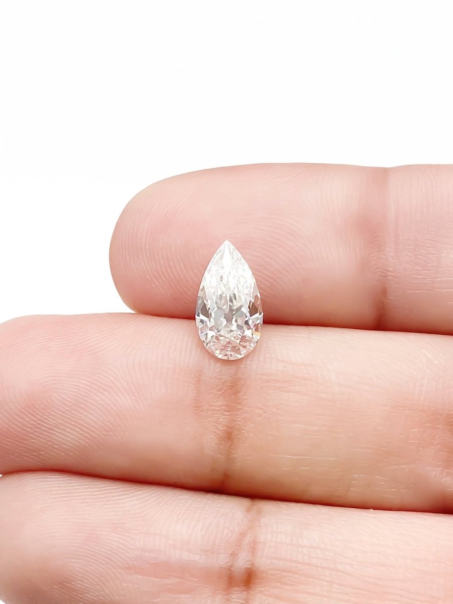 Teardrop-shaped diamond held between two fingers on a white background for scale