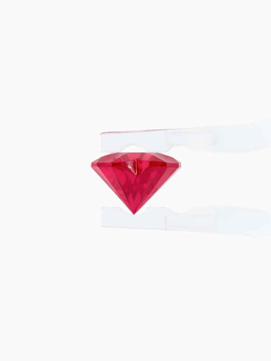 profile of red sapphire held by tweezers on white background