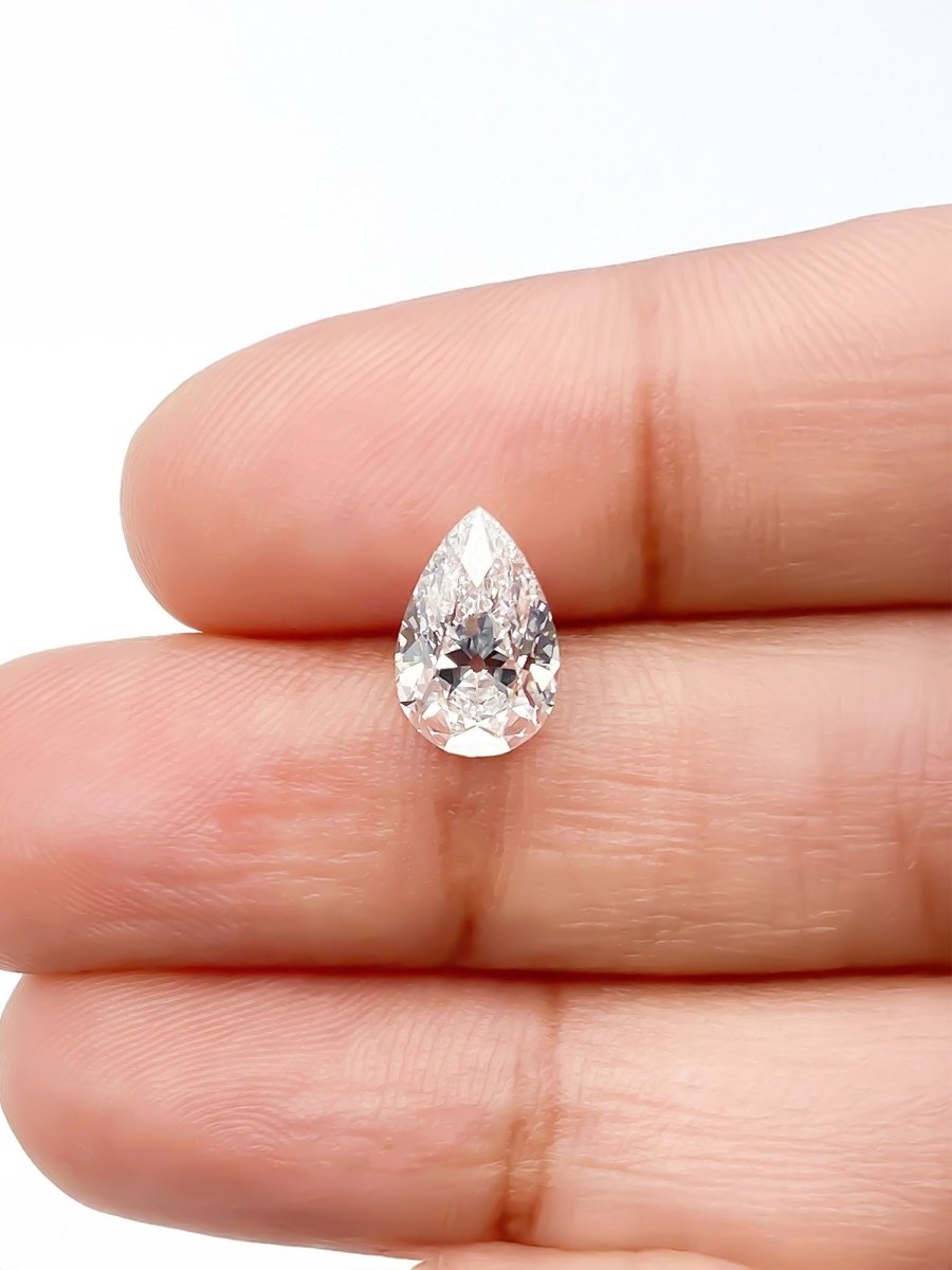 Pear-shaped diamond held between two fingers on a white background for scale