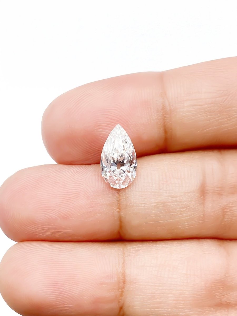 Pear-shaped diamond held between fingers on a white background for scale