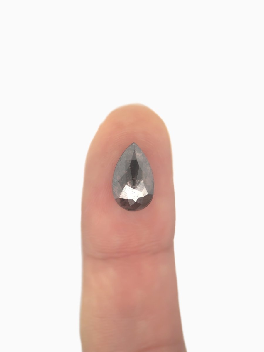 face view of loose lab-grown pear salt pepper diamond gemstone on fingertip for scale