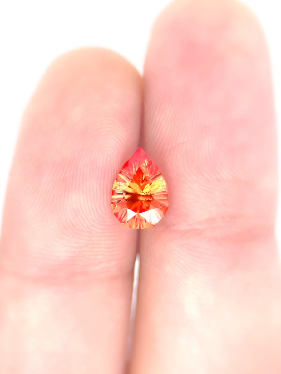 Orange sapphire pear held between two fingers against a white background for scale