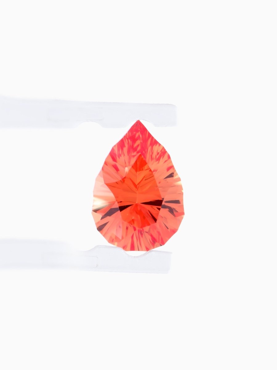 face view of designer cut orange pear sapphire held between tweezers on a white background