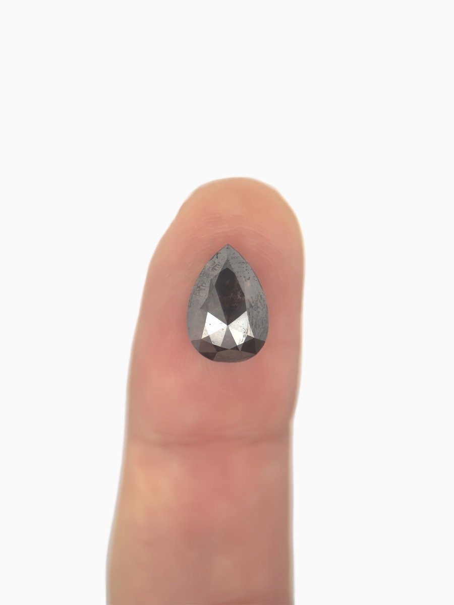 face view of loose lab-grown pear salt pepper diamond gemstone on fingertip for scale