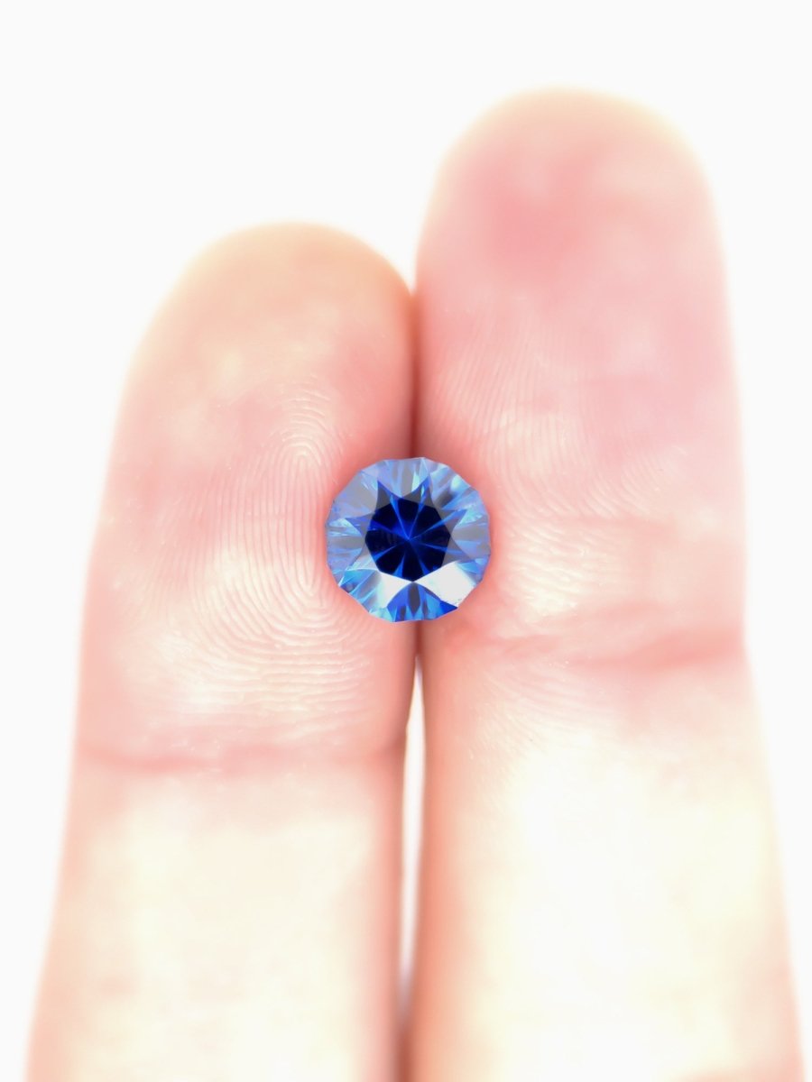 Blue sapphire held between two fingers against a white background for scale