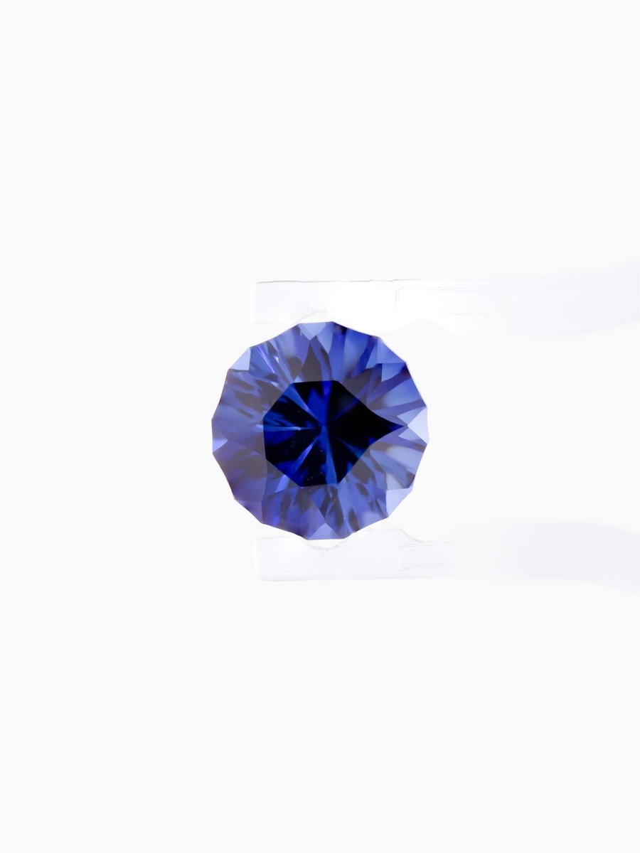face view of designer cut blue round sapphire held between tweezers on a white background