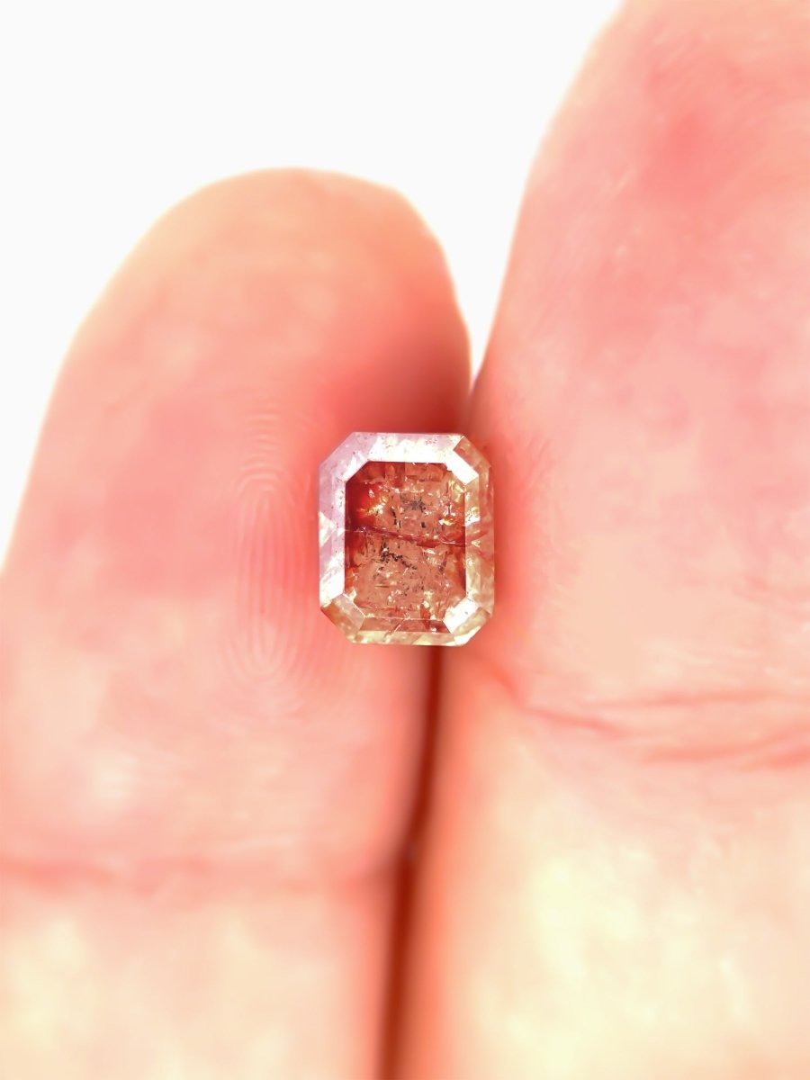 face view of loose emerald-cut rose salt pepper diamond gemstone on finger for scale