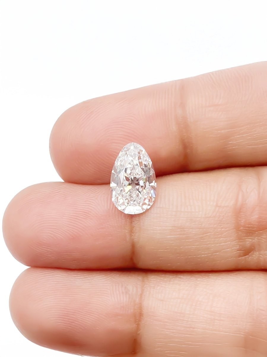Pear-shaped diamond held between two fingers on a white background for scale