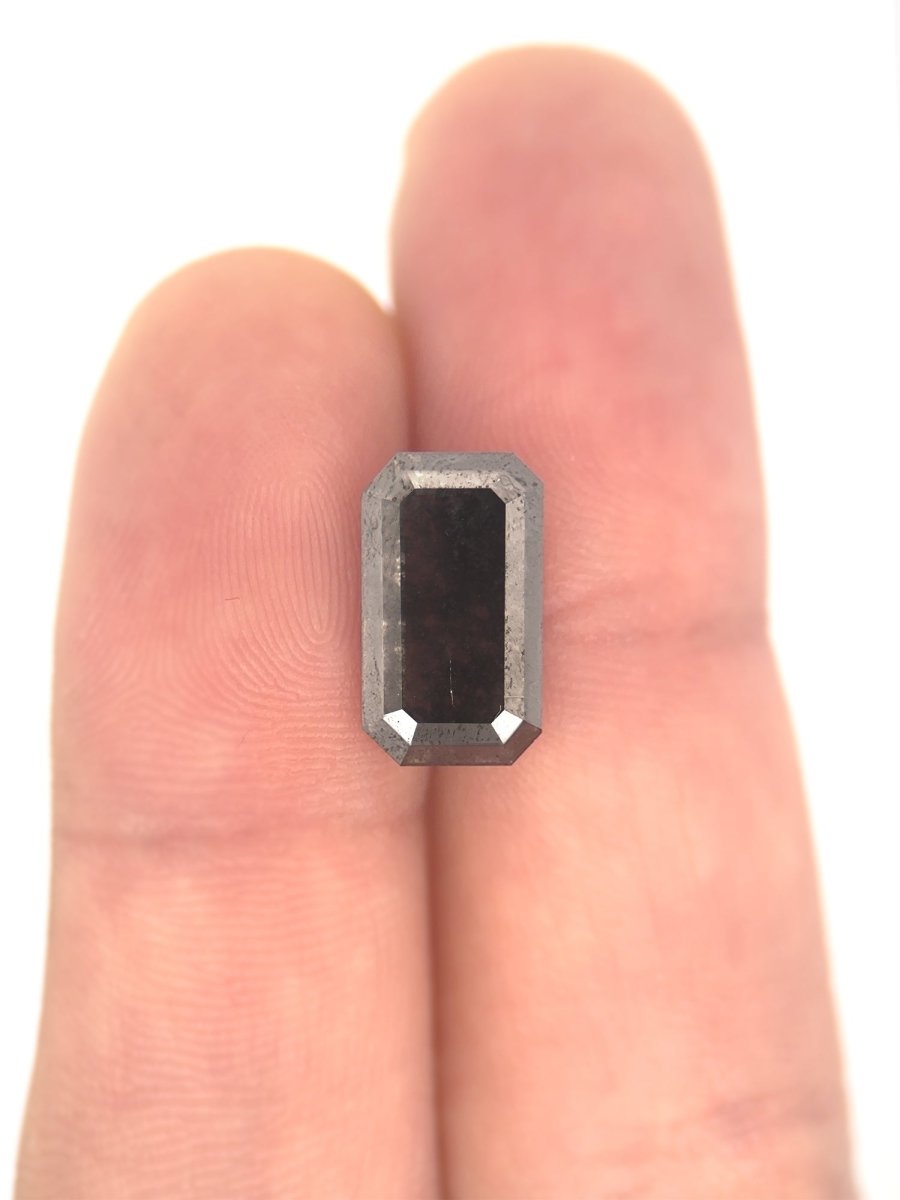 face view of loose lab-grown emerald-cut salt pepper diamond gemstone on finger for scale