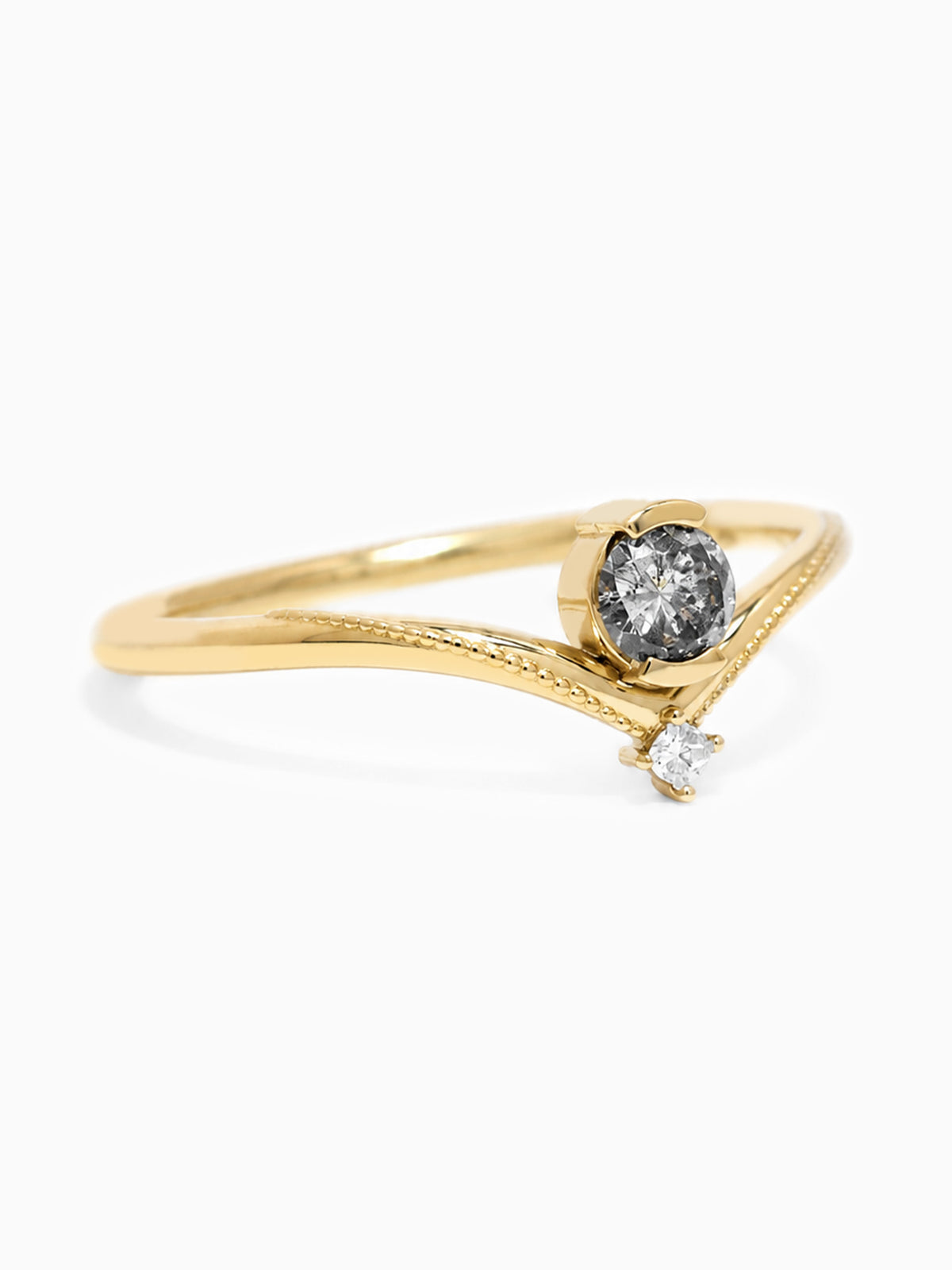 A gold ring with a curved, textured band, featuring a large round dark gemstone in the center and a smaller clear gemstone hanging from the lower tip, set against a plain white background.