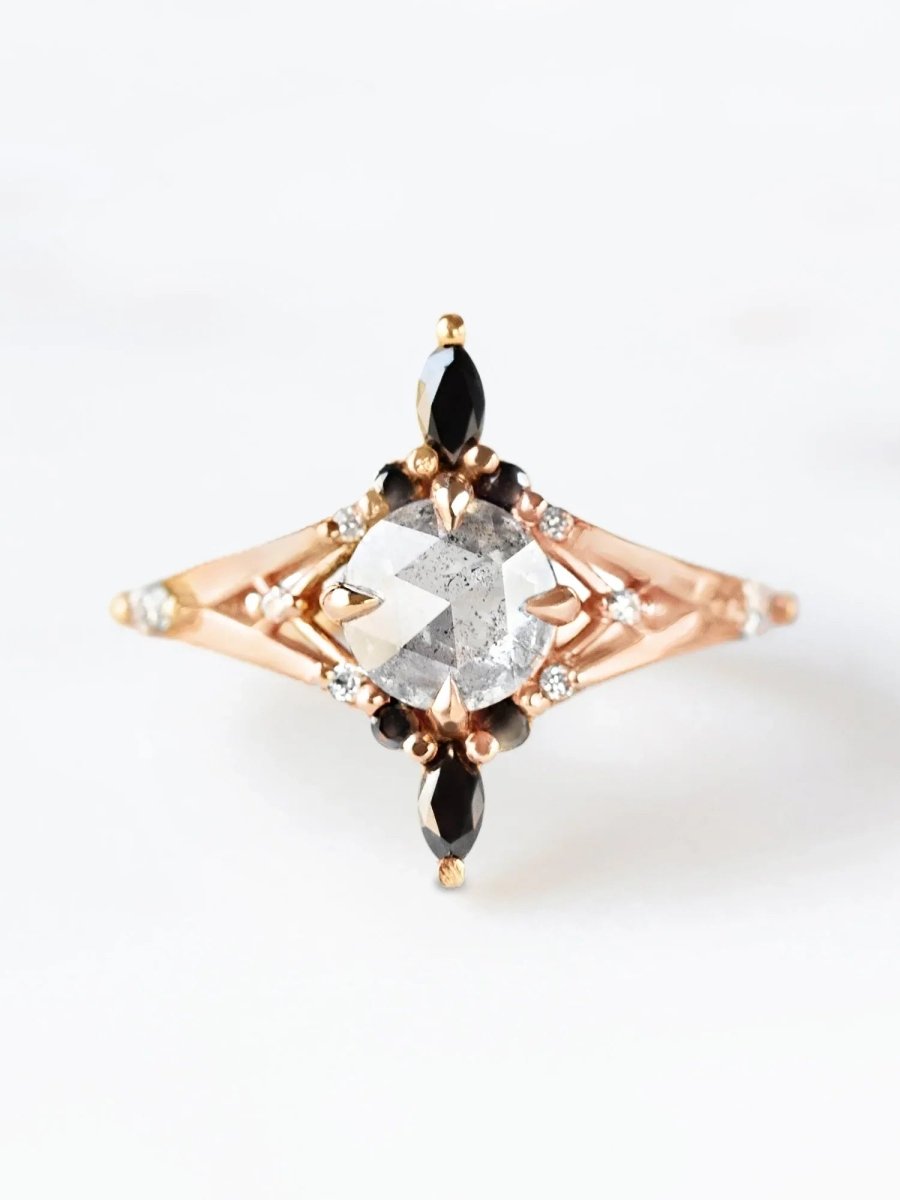 A bold engagement ring featuring black marquise-shaped diamonds around a central salt and pepper round diamond, with a geometric filigree band.