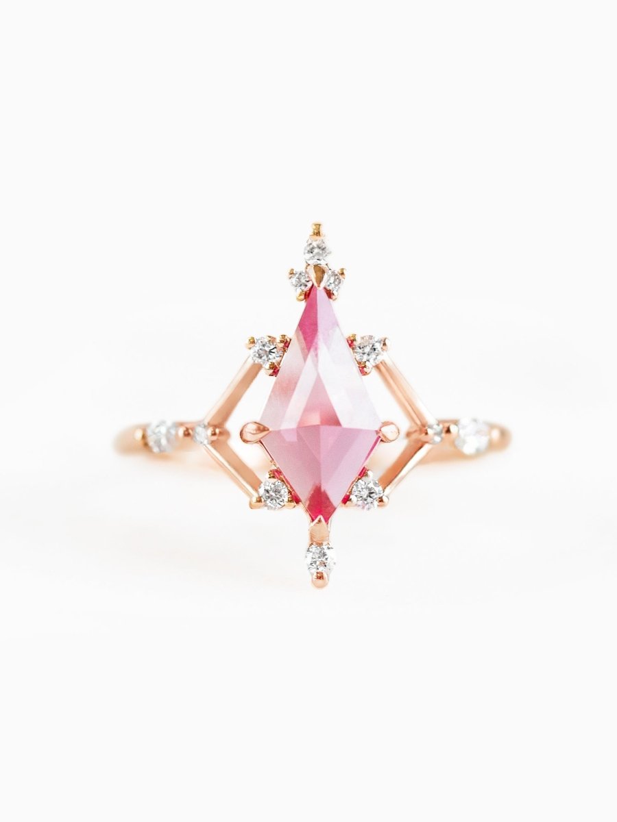 A gold ring featuring a large pink sapphire centerpiece with round white diamonds accents along the band and a geometric design.