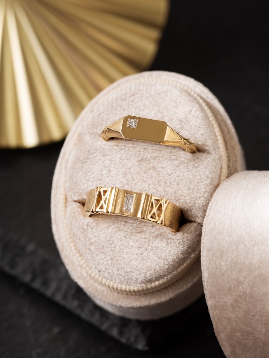 Two gold rings with diamond accents on a textured surface