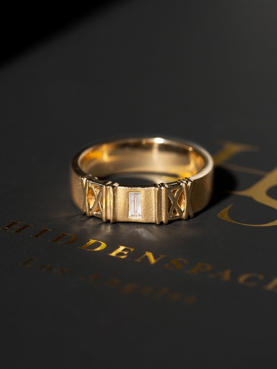 Gold ring with intricate design on dark grey hidden space packaging