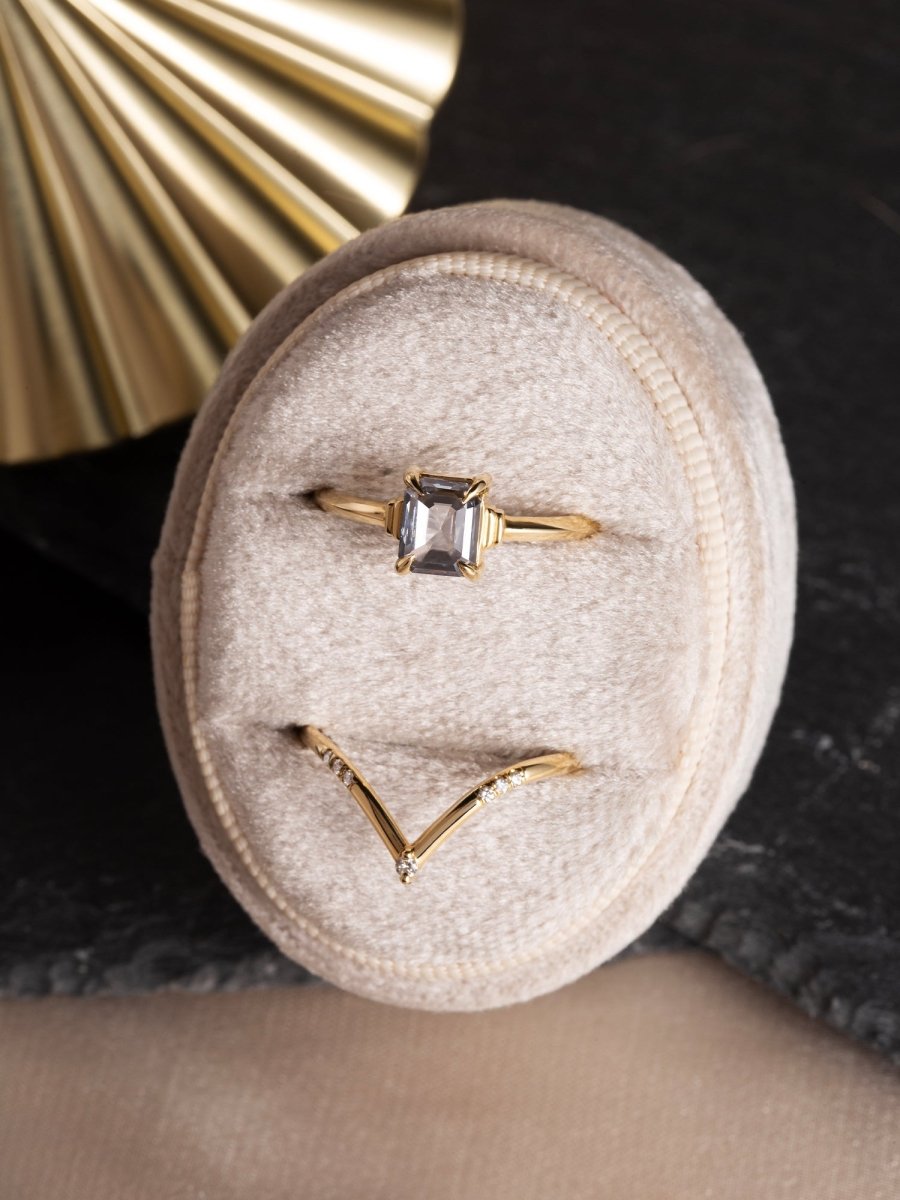 Gold ring with a diamond on a beige jewelry cushion against a dark background