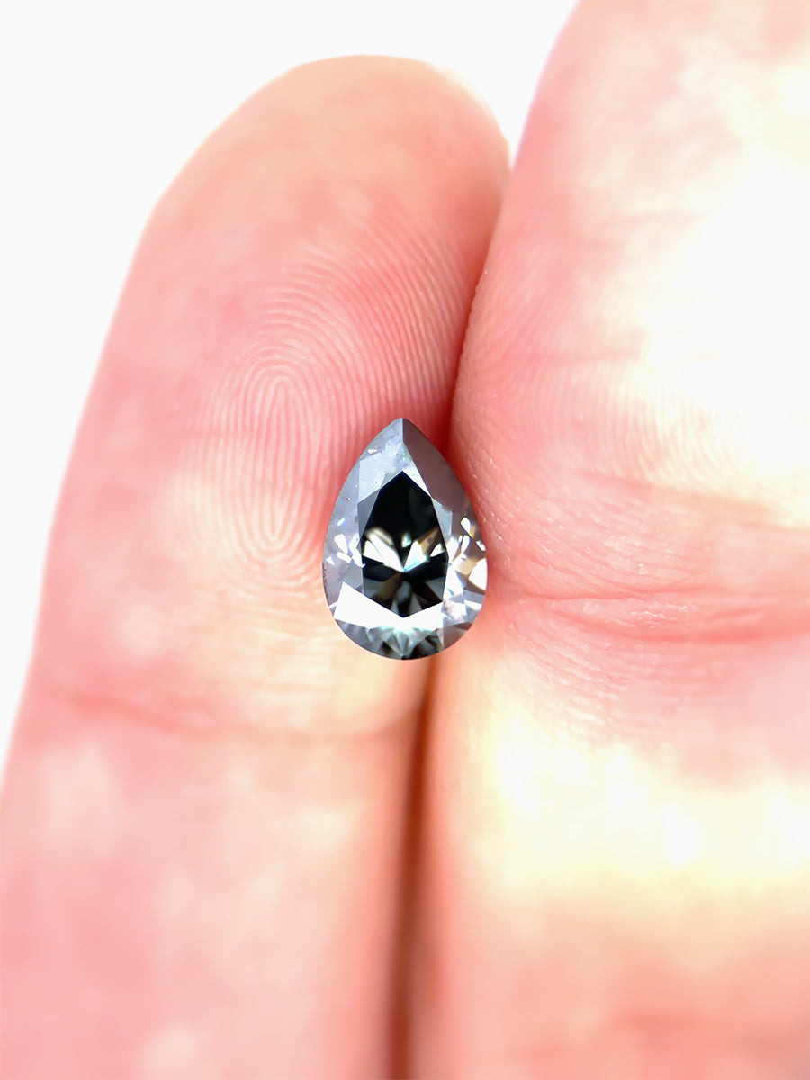 Black Pear Shaped Moissanite on White Background Held on fingers for scale