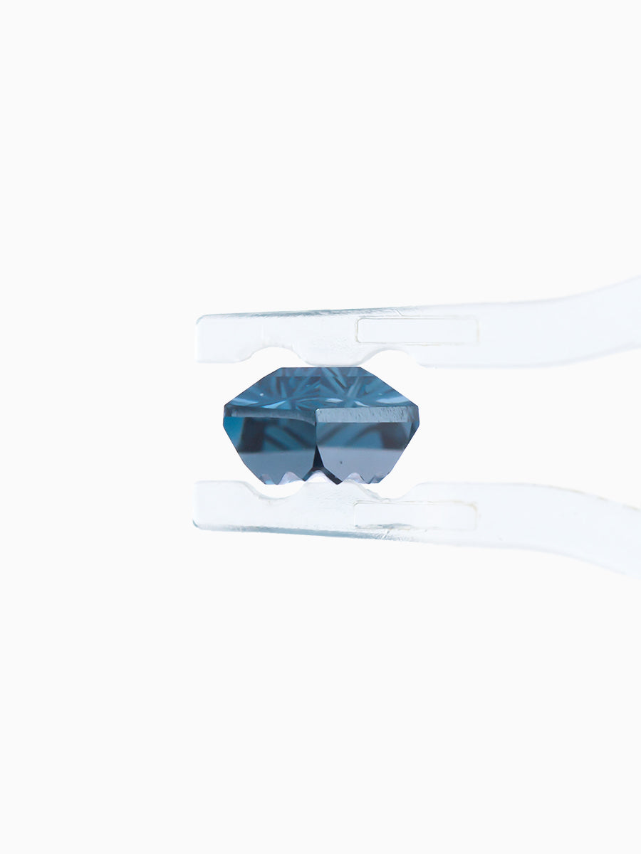 lab grown fantasy cut deep blue topaz hexagon held by tweezers, profile view