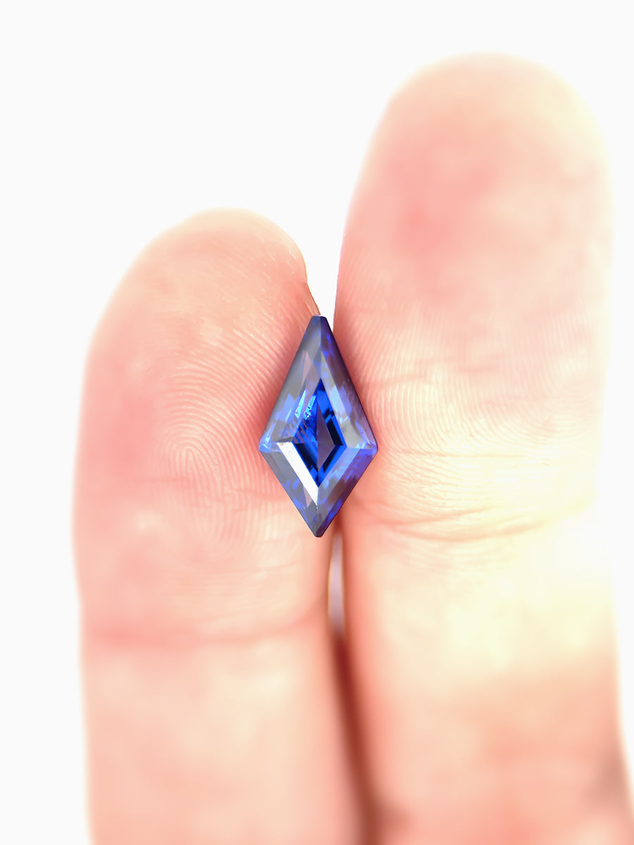 deep royal blue sapphire kite placed on finger for scale