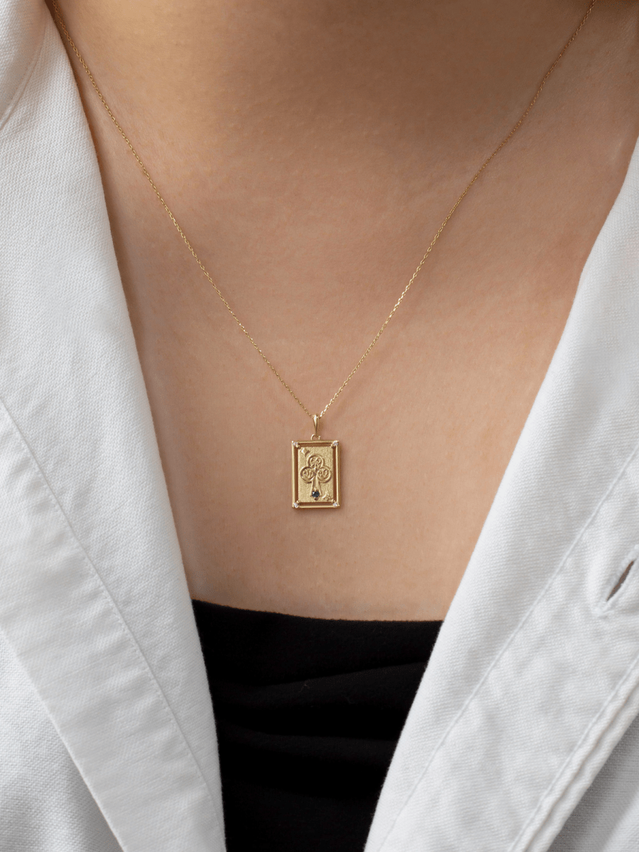 chest wearing rectangular playing card charm with embossed gold ace of clubs illustration and birthstone accent