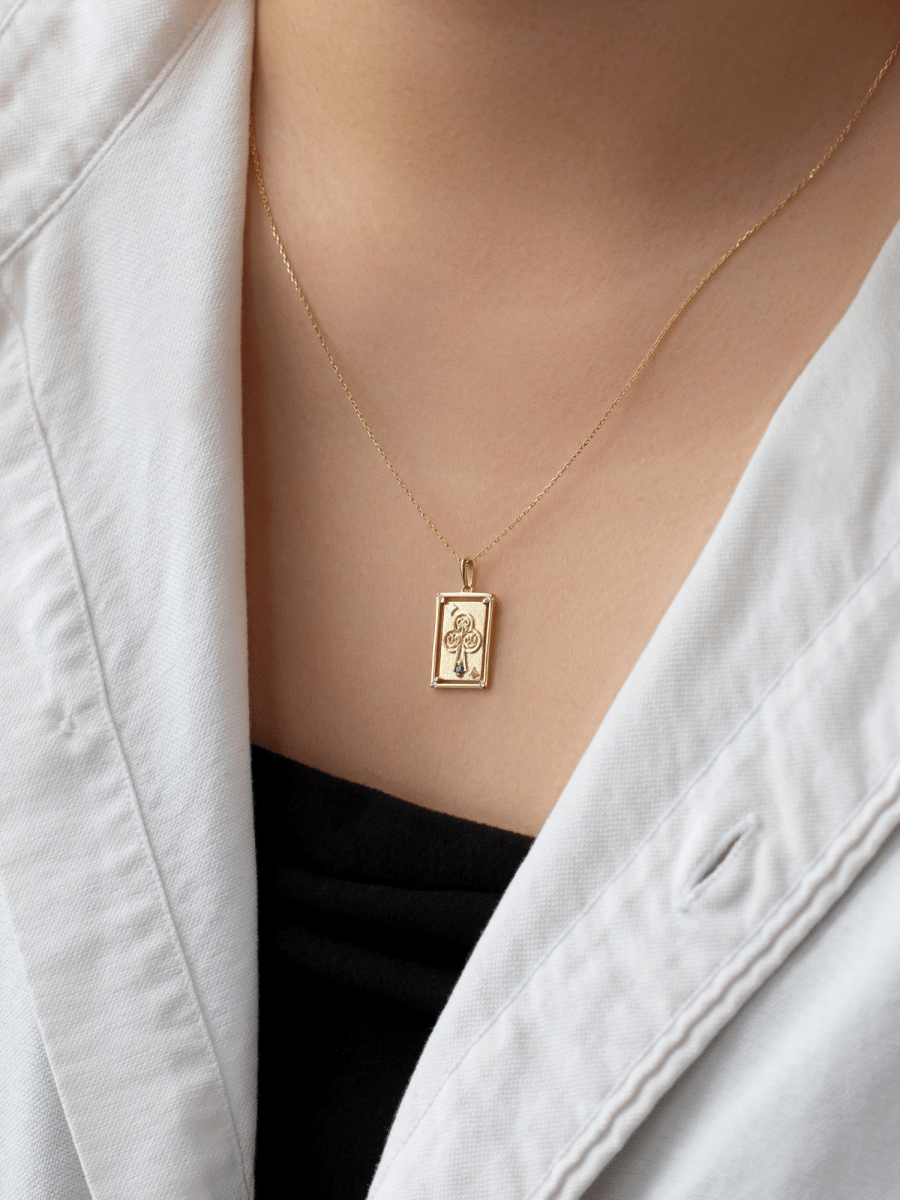 chest wearing rectangular playing card charm with embossed gold ace of clubs illustration and birthstone accent
