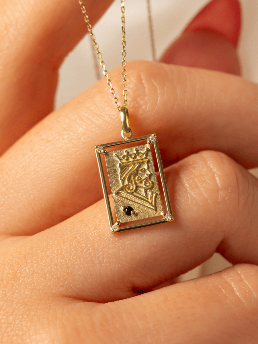 Close-up of hand holding rectangular playing card charm with embossed gold king illustration and birthstone accent on chain