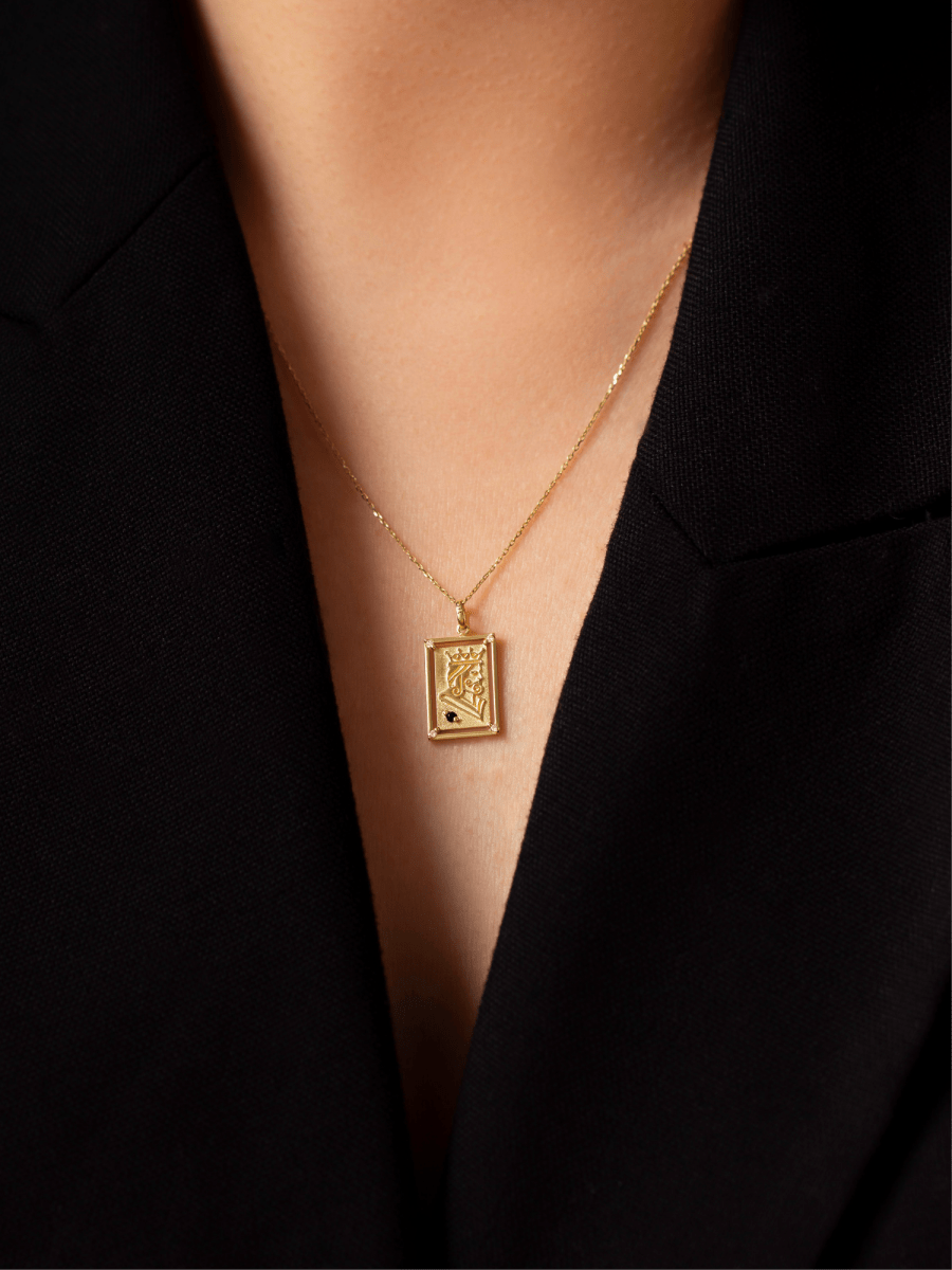 Chest wearing rectangular playing card charm with embossed gold king illustration and birthstone accent