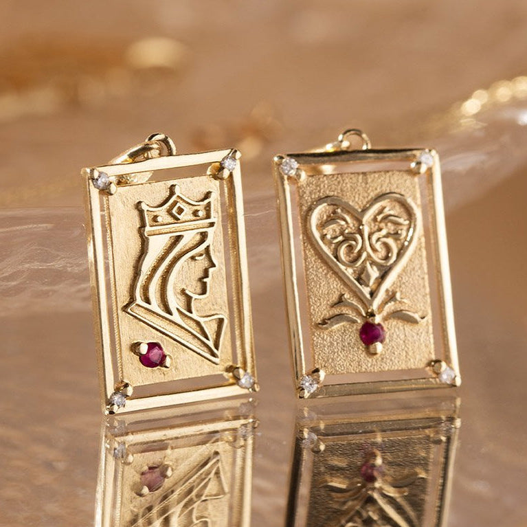 Gold earrings with intricate designs and red gemstones on a reflective surface.