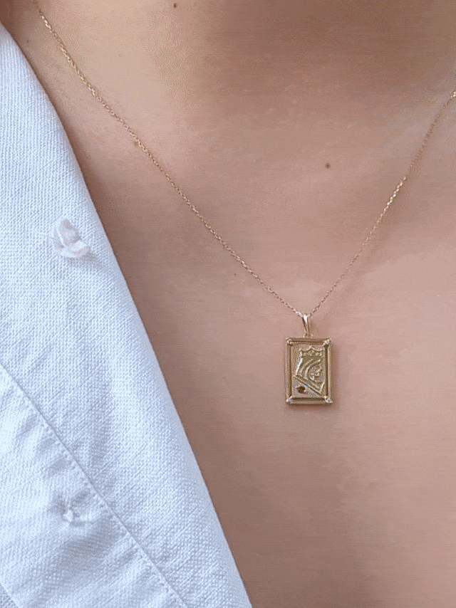 GIF of chest wearing rectangular playing card charm with embossed gold queen illustration and birthstone accent