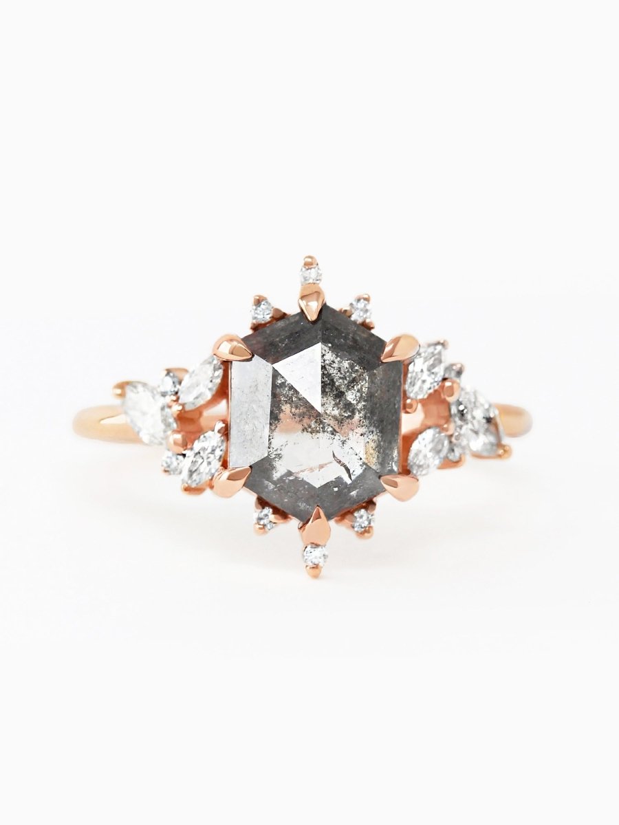 A rose gold engagement ring with a hexagon-shaped salt and pepper diamond centerpiece, surrounded by clusters of marquise-cut diamonds.