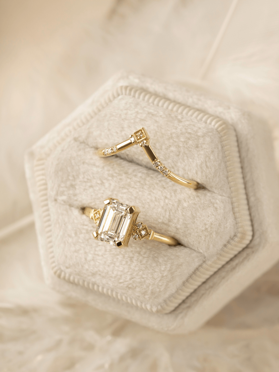 Two gold rings with gemstones in a hexagonal jewelry box on a soft beige background