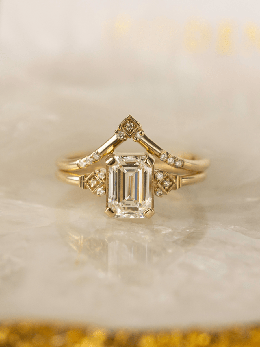 Gold ring with emerald-cut diamond on a soft beige background