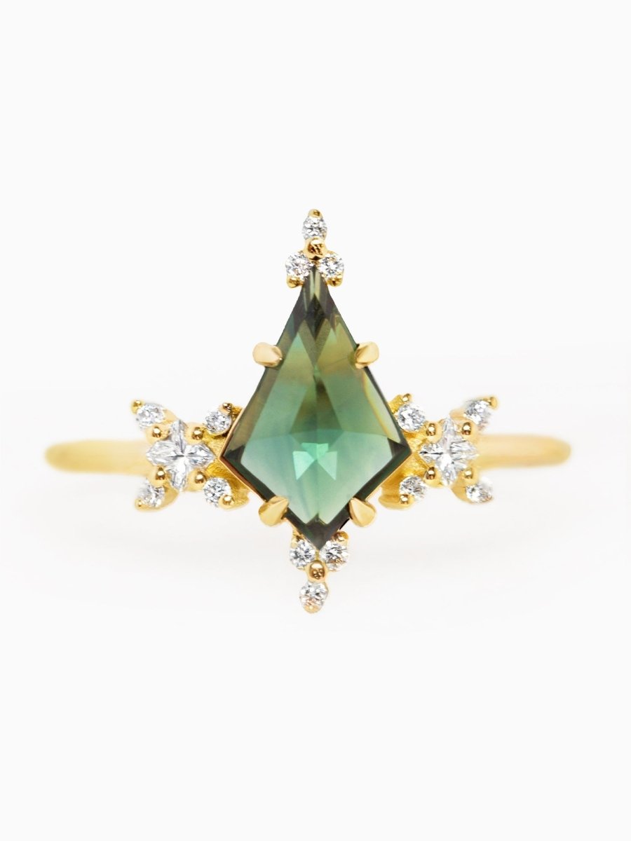 A gold ring with a large green sapphire centerpiece surrounded by smaller decorative stones set in a kite-shaped design.