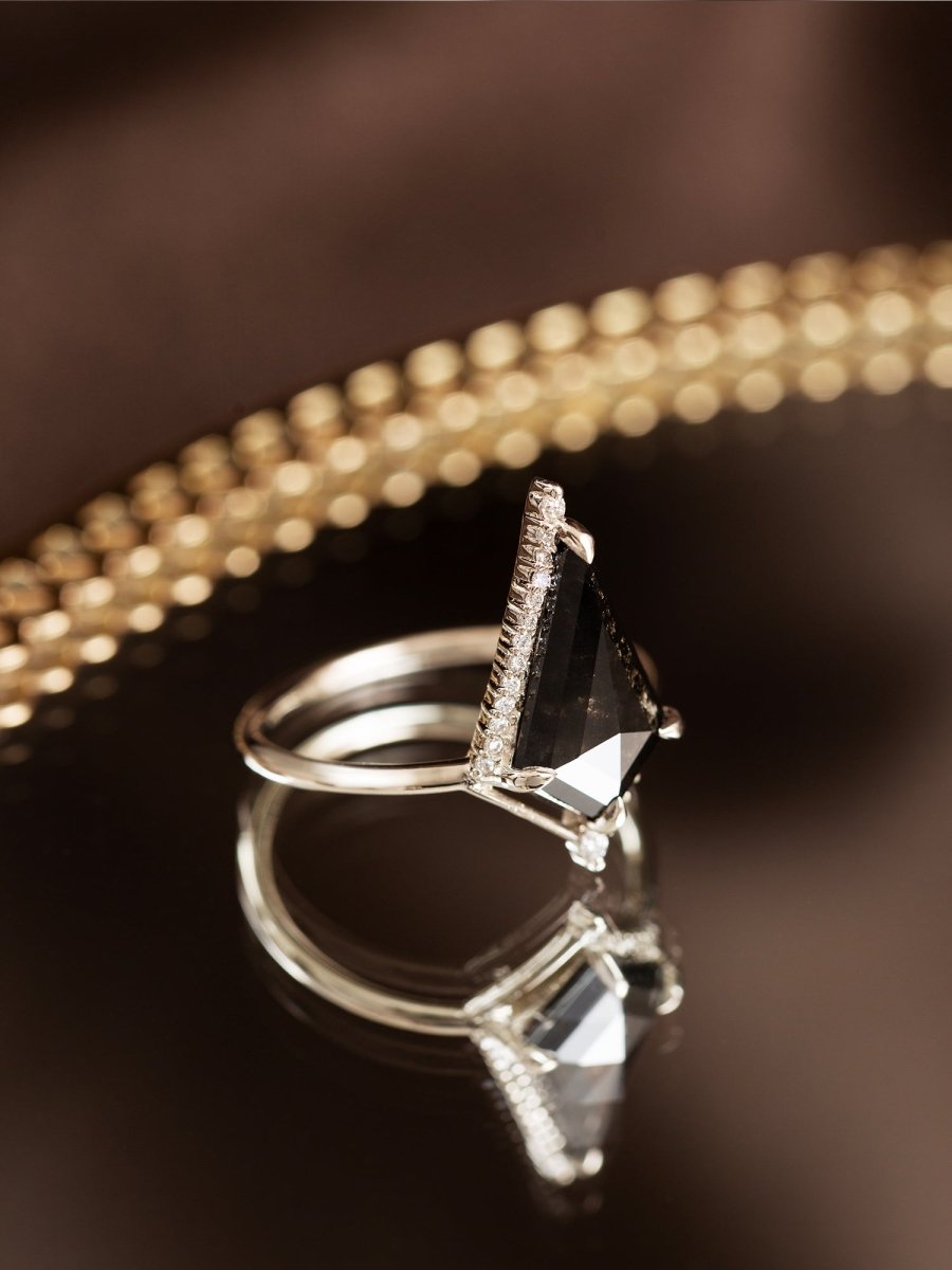 Silver ring with a black gemstone on a reflective surface