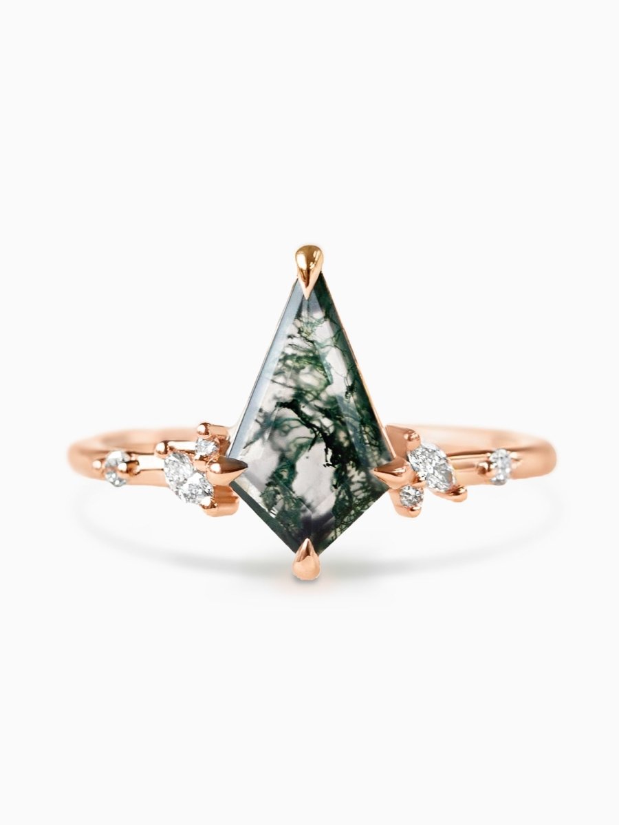 A rose gold ring with a kite-shaped Moss Agate center stone, accompanied by smaller diamond-like stones on the sides.