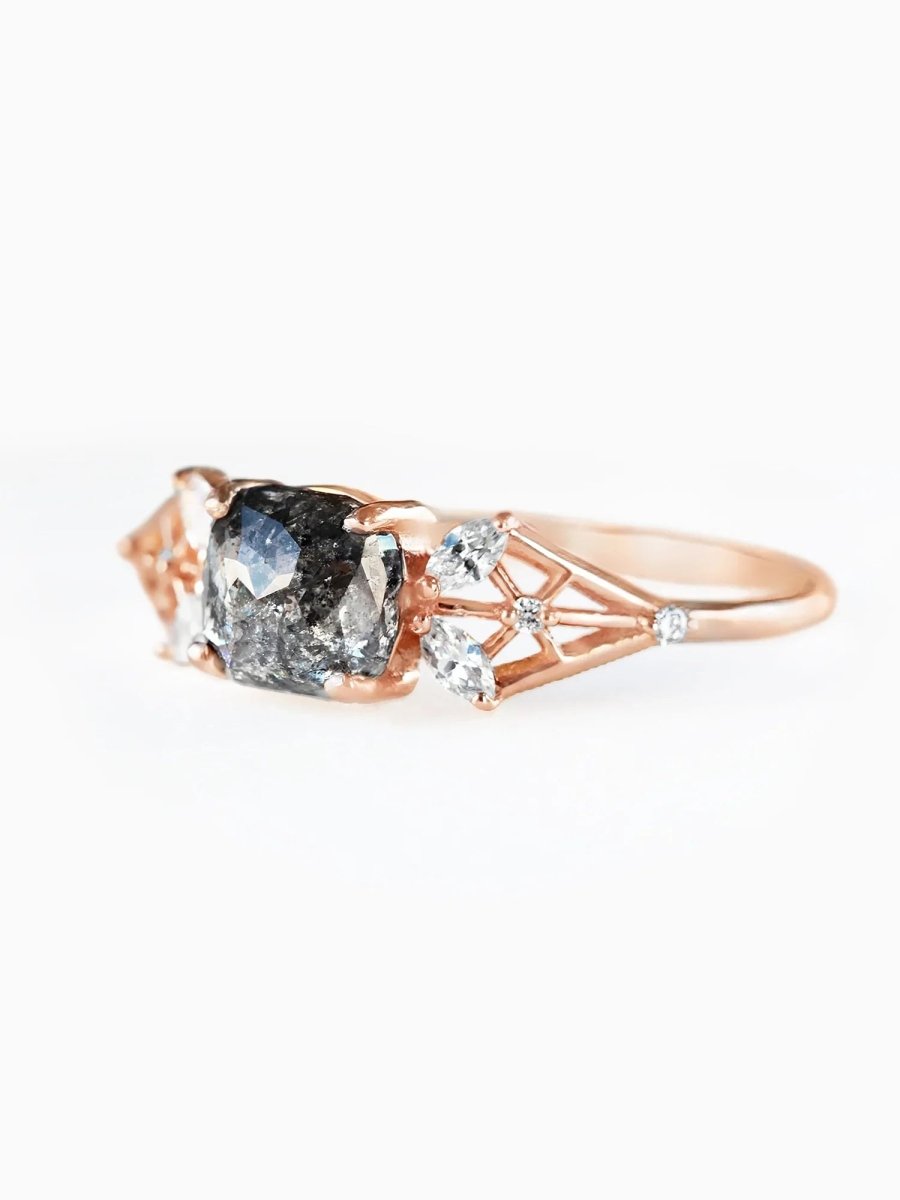 Rose gold ring with a large dark stone and smaller clear stones on a white background