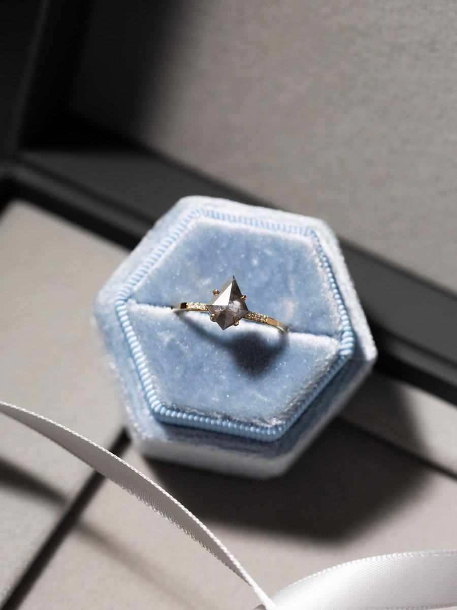 Hexagonal blue velvet box with a diamond ring on a gray surface