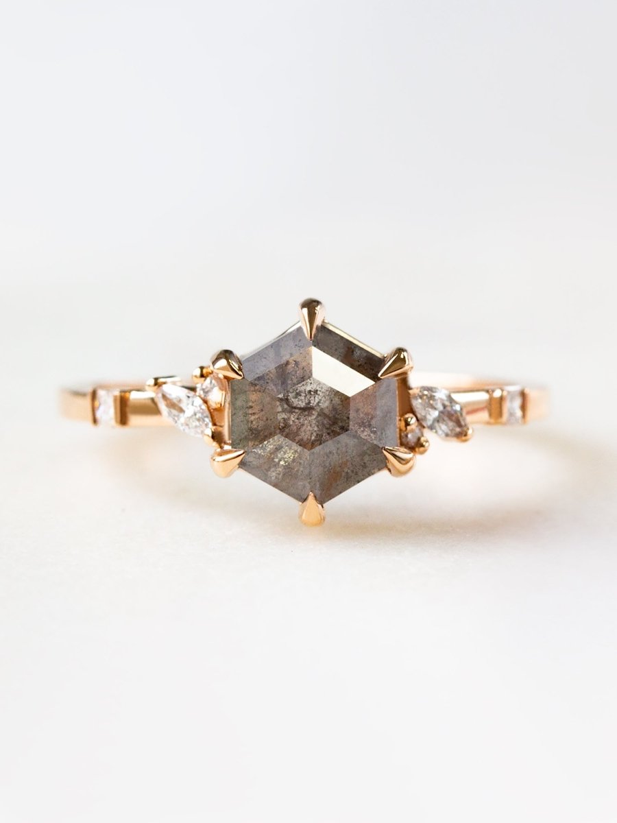 A unique engagement ring featuring a hexagon-shaped salt and pepper diamond with asymmetrical side stones set in a gold band.