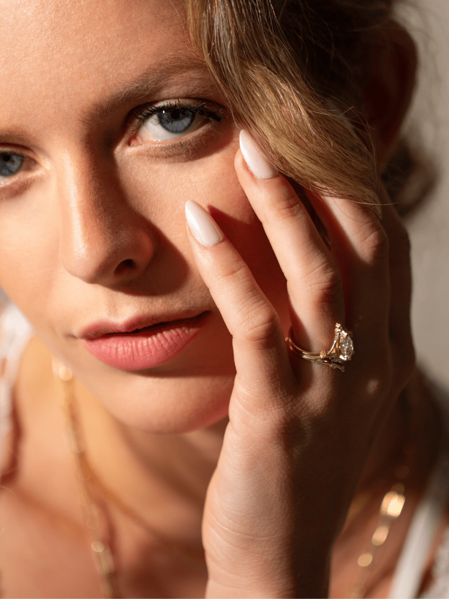 Woman looking into camera with hand on face, wearing Art Nouveau marquise diamond ring and chevron band