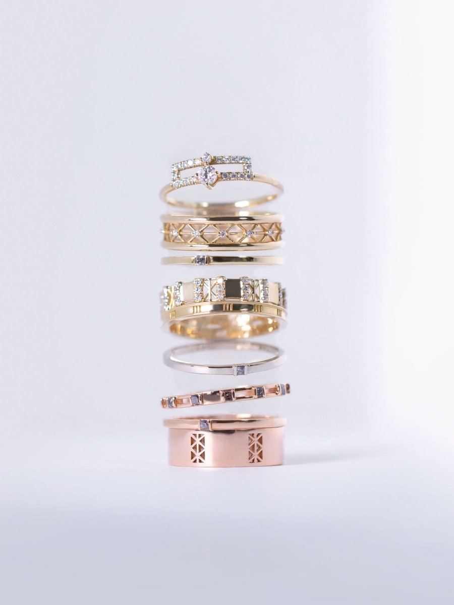 A collection of various rings and a band, with intricate designs, displayed stacked on top of each other.