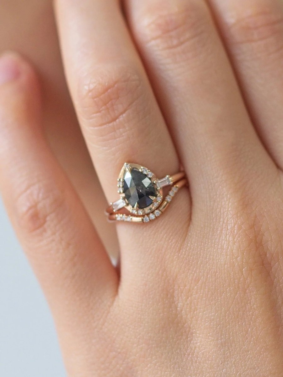 Pear-shaped salt and pepper diamond engagement ring in 14k rose gold inspired by the art deco style and minimalism on model's hand.