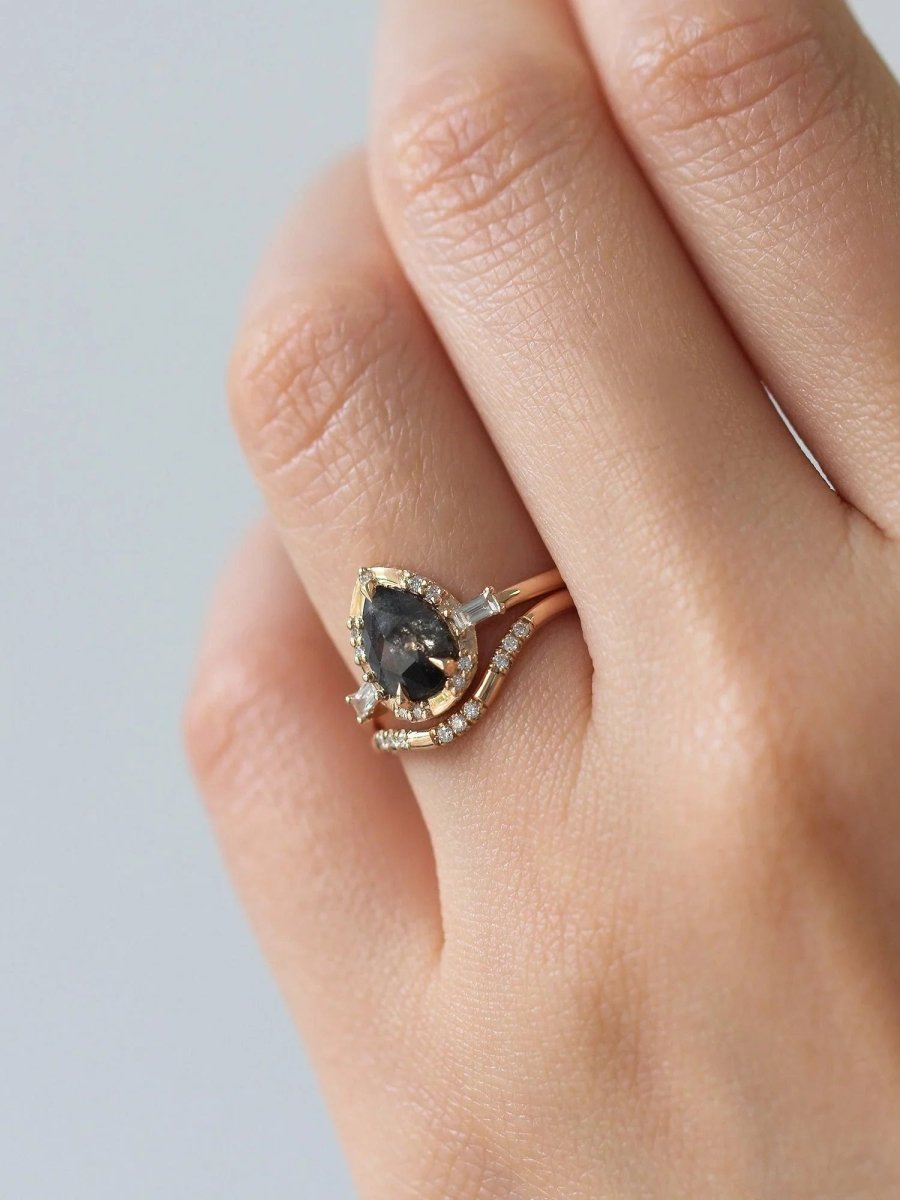 Pear-shaped salt and pepper diamond engagement ring in 14k rose gold inspired by the art deco style and minimalism on model's hand.