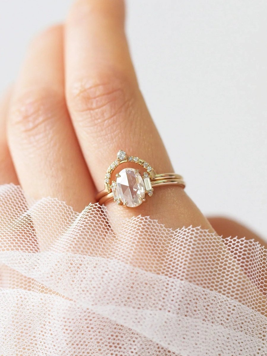 Gold ring with a white gemstone on a person's finger wearing a sheer pink fabric.