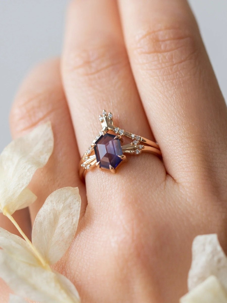 Rose gold ring with a purple gemstone on a hand with white flowers in the background