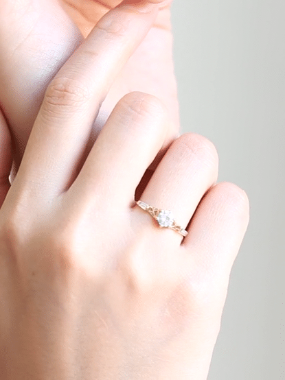 GIF of hand wearing round white diamond ring with flared shoulders and art deco lattice detail