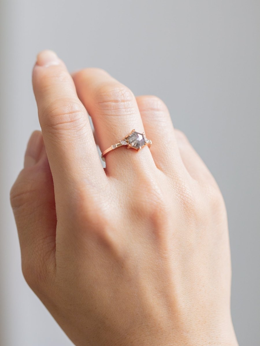 Unique art deco styled hexagon shaped salt and pepper diamond engagement ring in 14k rose gold with smaller marquise, round, and princess cut diamonds on model's hand.