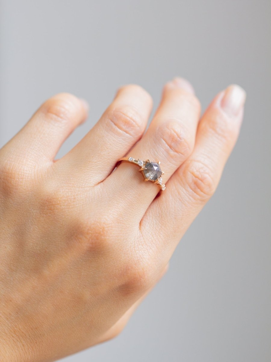Unique art deco styled hexagon shaped salt and pepper diamond engagement ring in 14k rose gold with smaller marquise, round, and princess cut diamonds on model's hand.
